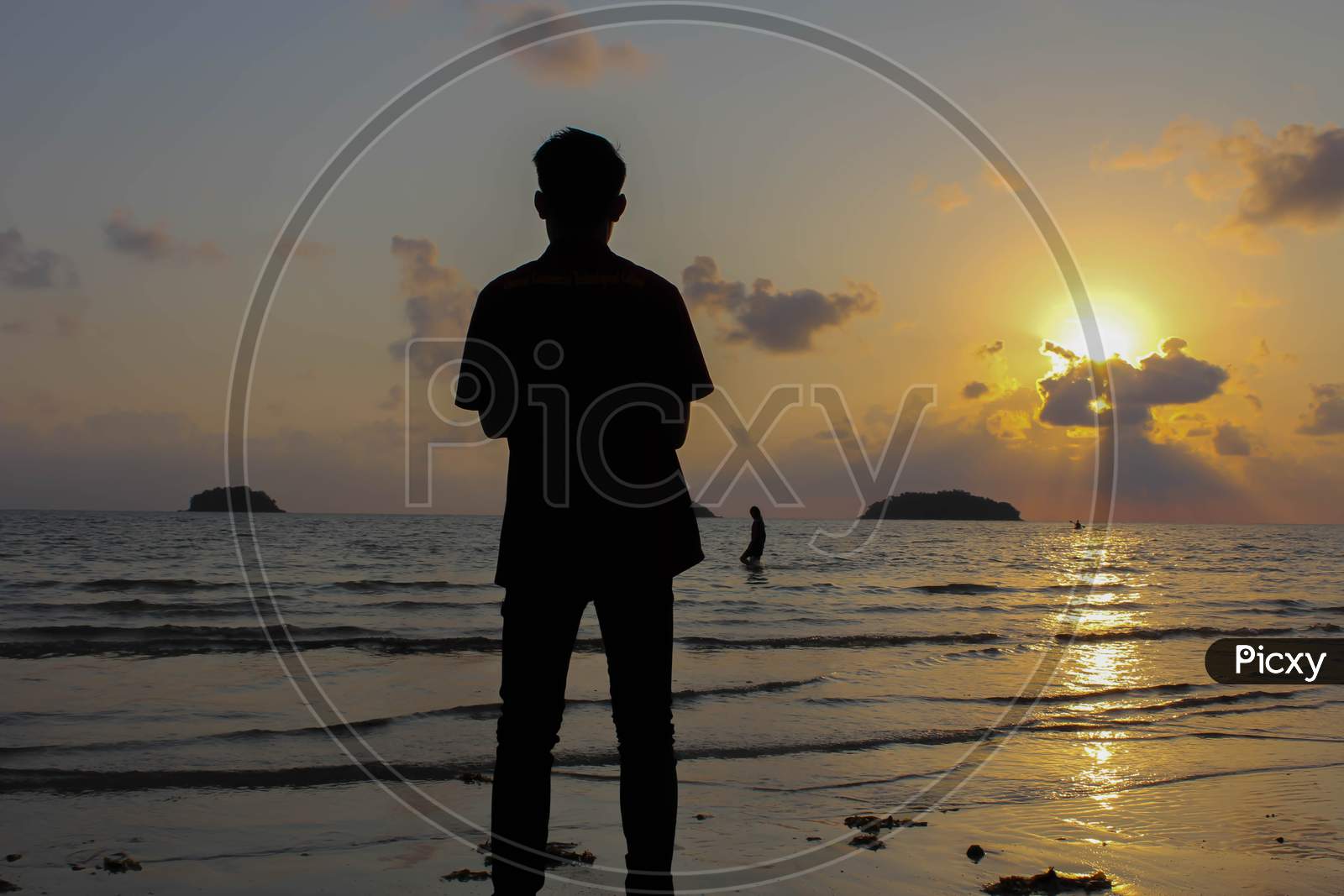 Lonely Man Stands On The Beach Looks Towards The Sun Light