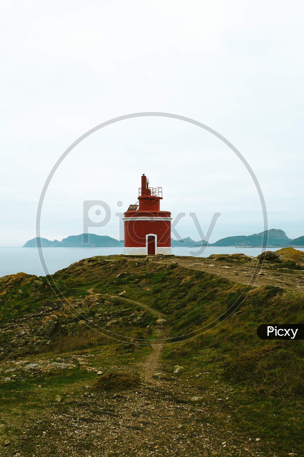 Red Lighthouse In The Coast Of Spain Over A Super Green Grass With A Clear Blue Sky With Copy Space