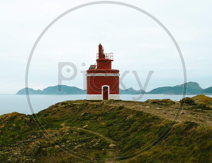 Red Lighthouse In The Coast Of Spain Over A Super Green Grass With A Clear Blue Sky With Copy Space