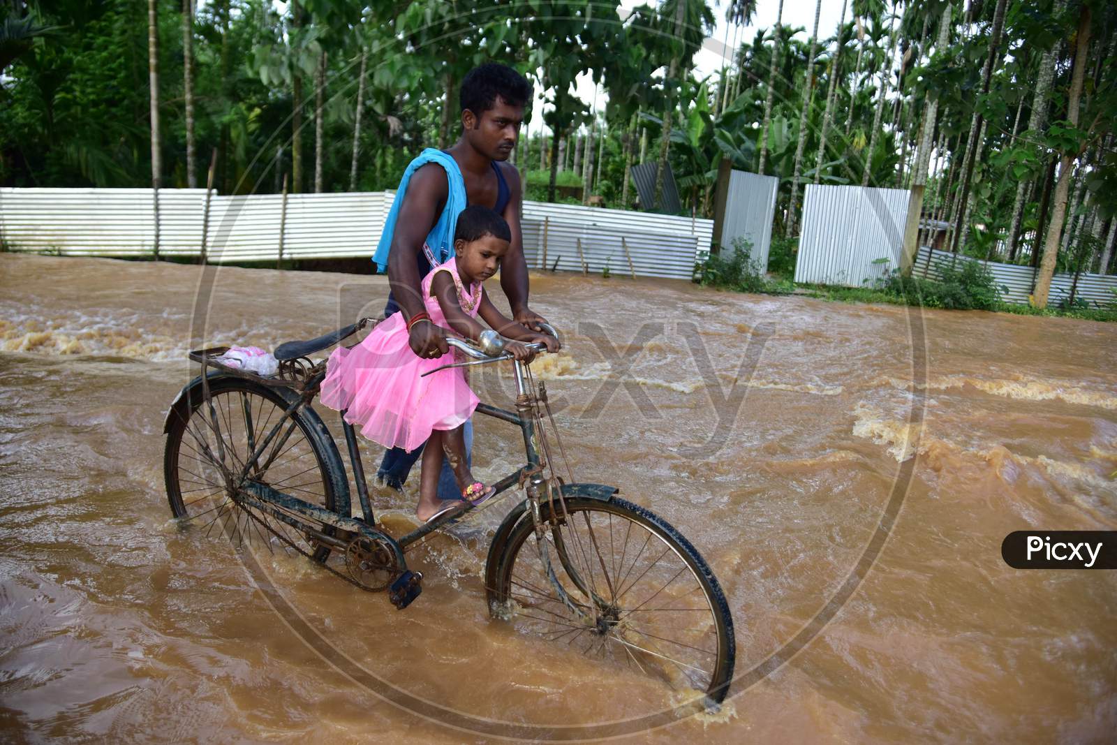 A man carries his daughter on a bicycle as he wades through a flooded area, following heavy rainfall, in Nagaon district, Sept. 25, 2020. (