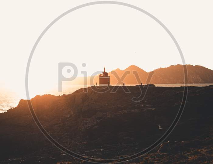Red Lighthouse Under A Massive Sunset In The Coastline Of Spain During A Super Bright Day