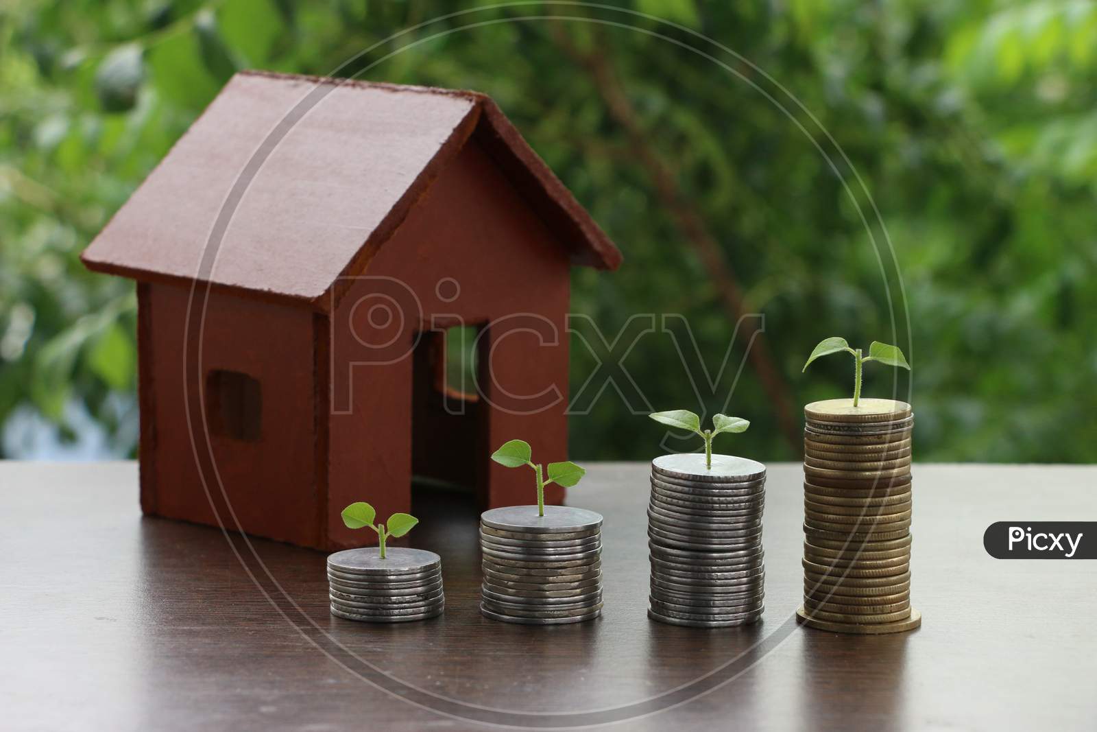 Model Of House With Money Coins Stack On Wooden Table On Blurred Background. Growing Money - Plant On Coins - Saving And Investment Concept.