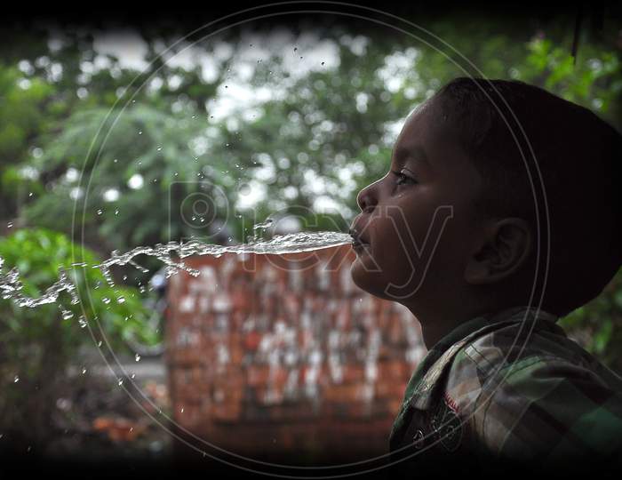 A South Asian boy splashing water from his mouth