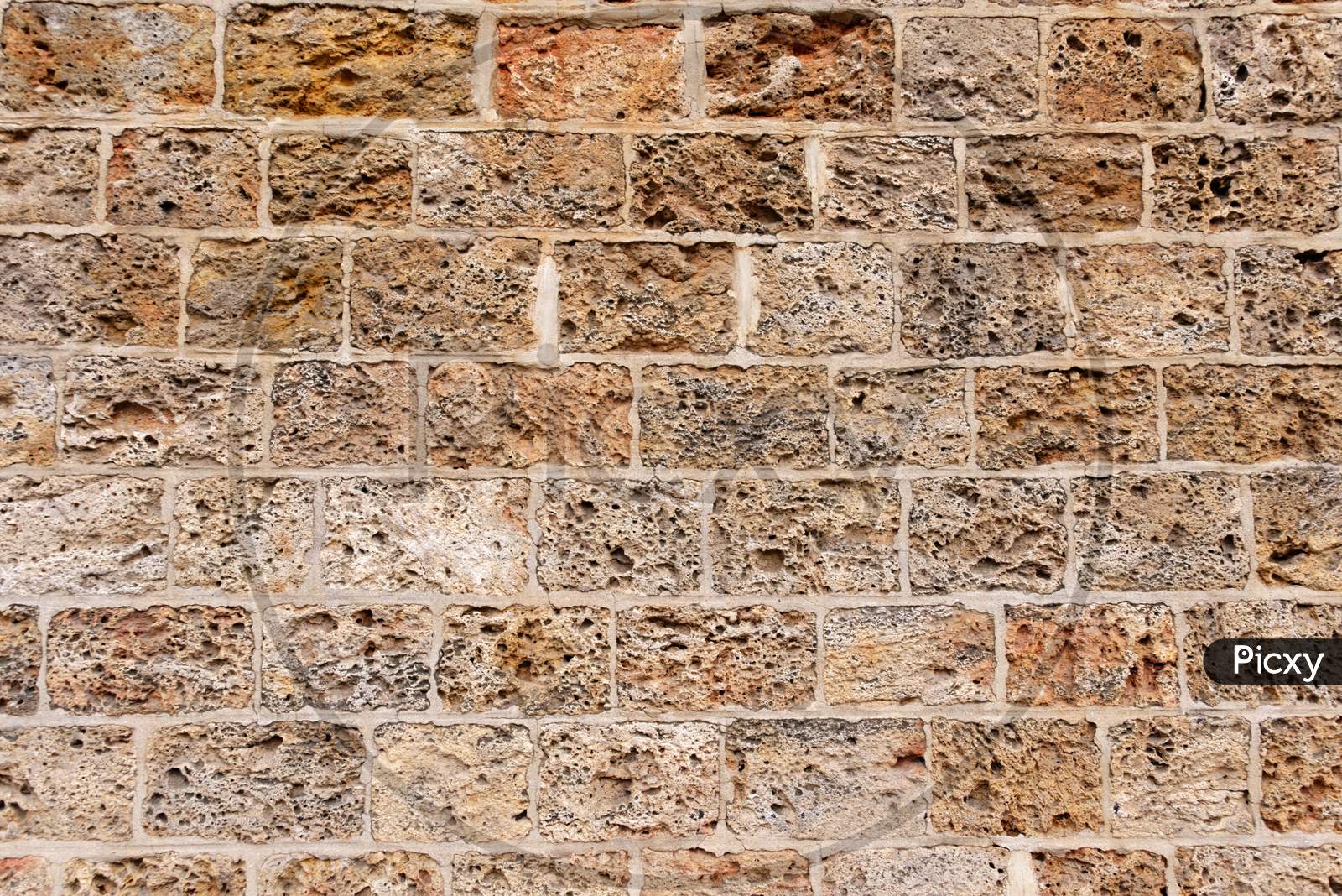 A Wall Formed By Spongy Textured Bricks Attached With Cement Solution Along With Different Color Tones