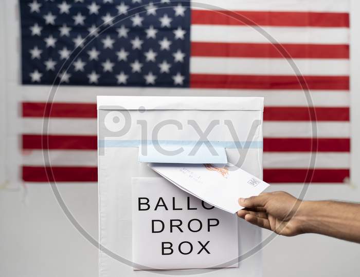 Maski, India 14 September, 2020 : Concept Of Mail In Vote At Us Election - Wide Angle Shot Of Hands Dropping Mail Inside The Ballot Box With Us Flag As Background.