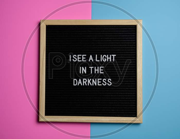 Motivational Quote "I SEE A LIGHT IN THE DARKNESS " Text In The Black Slate Behind pink & Blue Background.