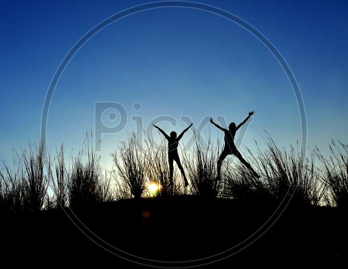 Silhouette of two boys jumping behind the grass grains