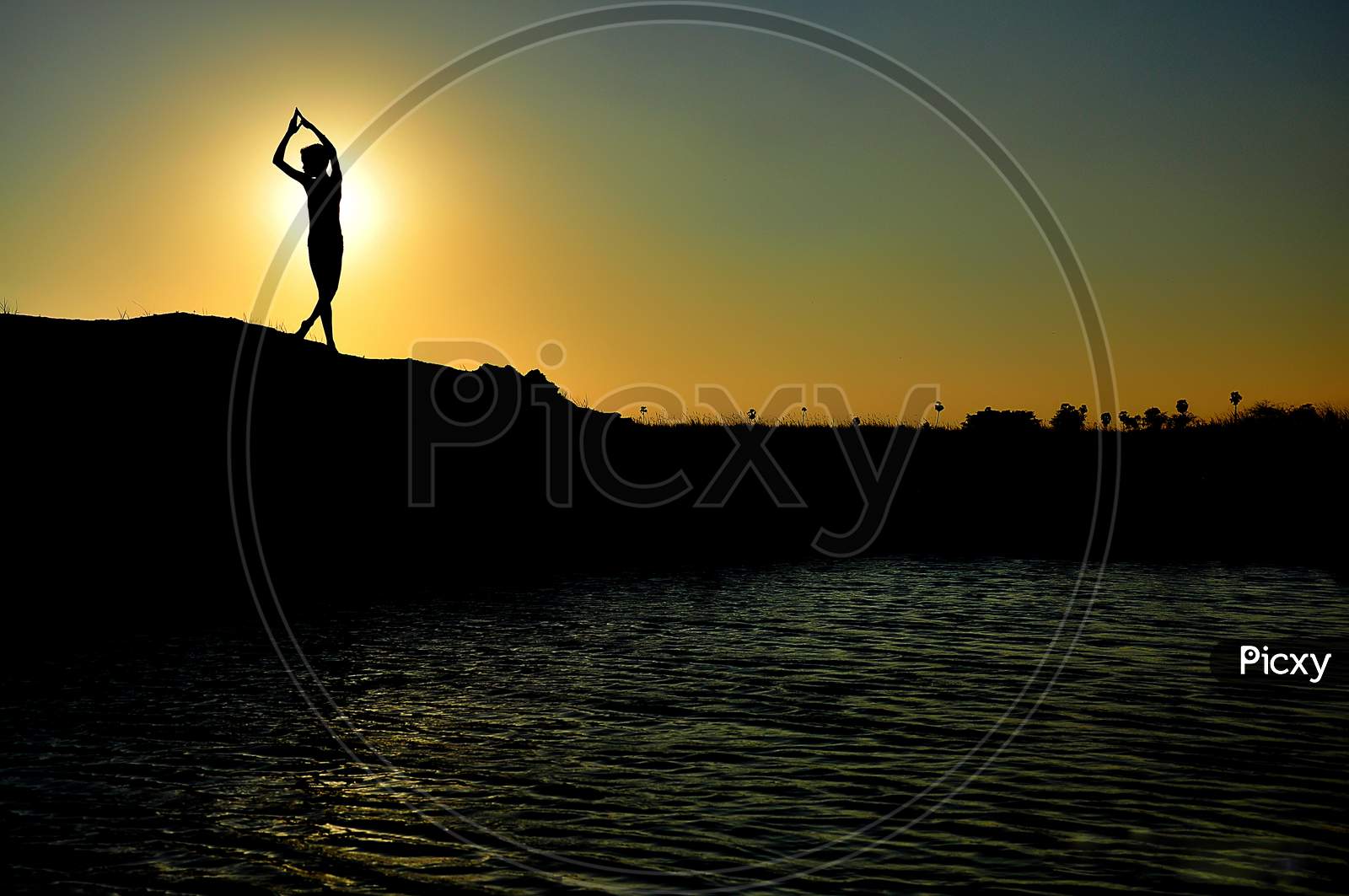 Silhouette of a boy doing yoga while the sunrise