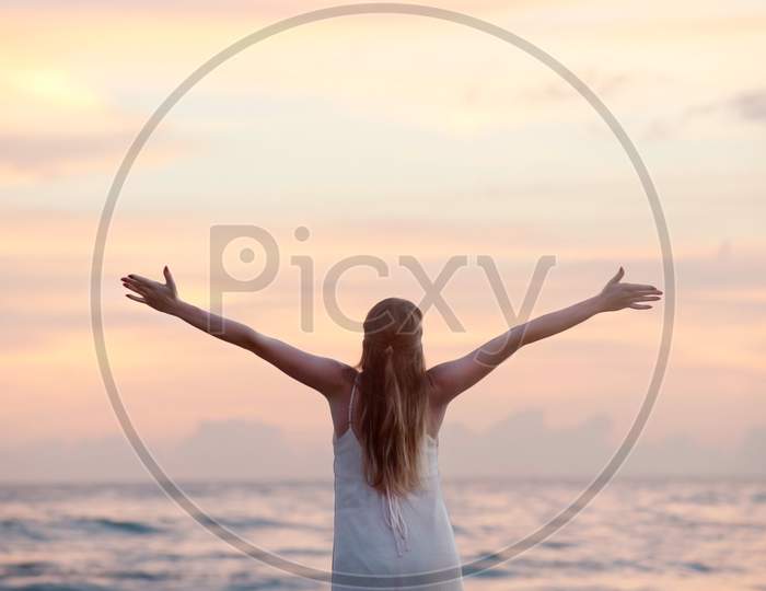 Rear View of Woman With Arms Raised at Beach during Sunset.