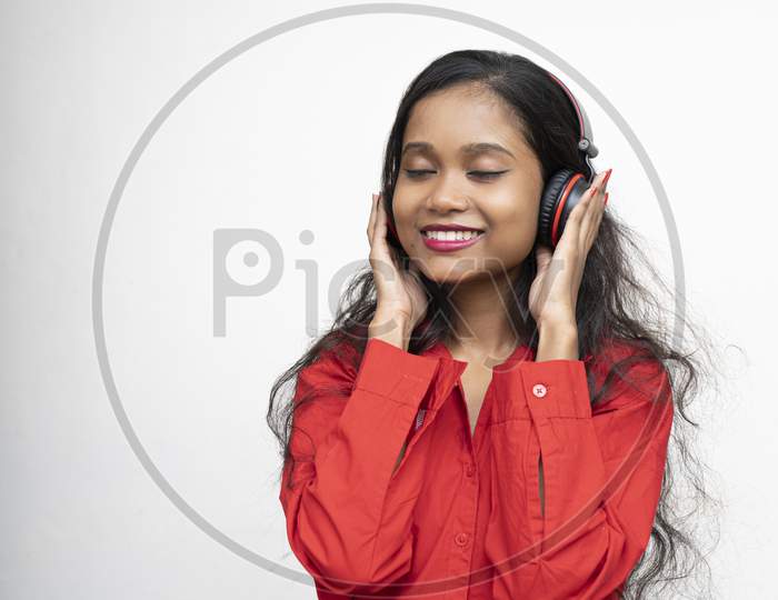Young Charming Girl In Red Shirt Listening To Songs In Her Headphones. White Background And Copy Space.