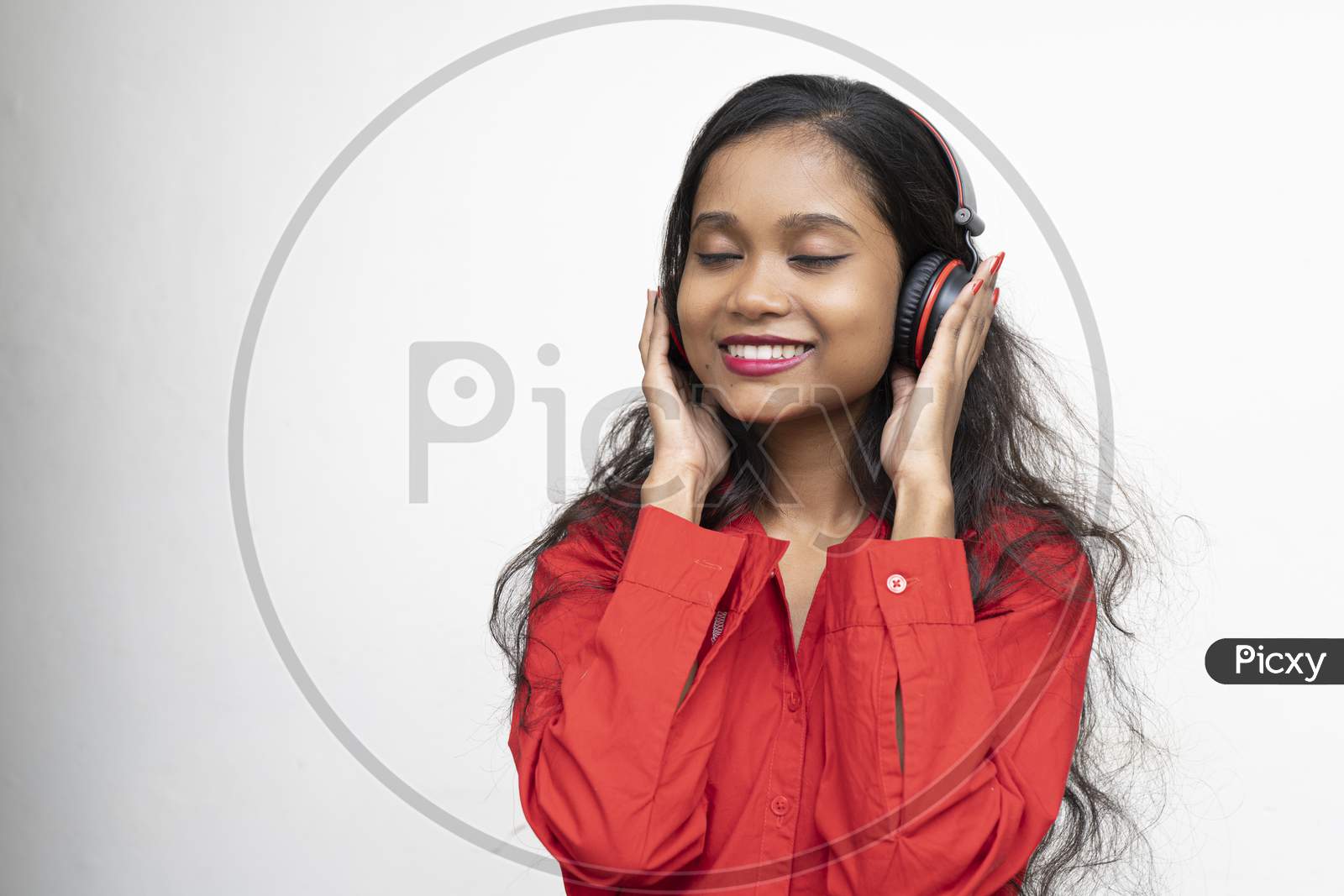 Young Charming Girl In Red Shirt Listening To Songs In Her Headphones. White Background And Copy Space.