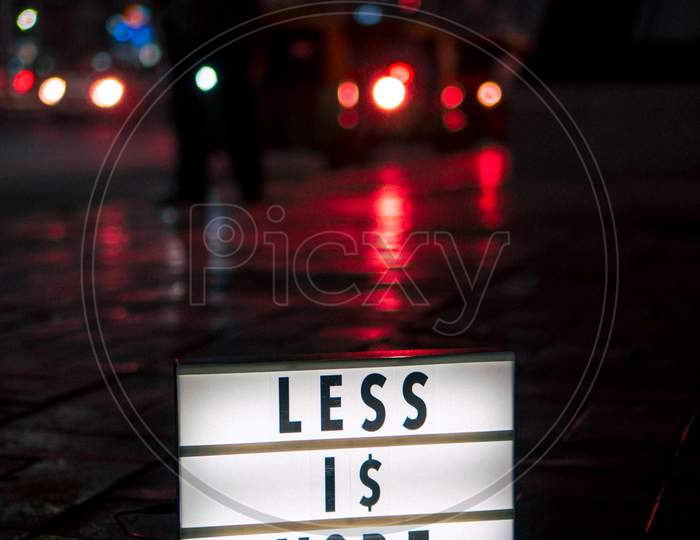 illuminated Motivational Signage of  Less 1$ More on Sidewalk.