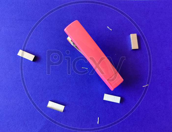 Pink Color Stapler And Stapler Pins Isolated On Blue Background.
