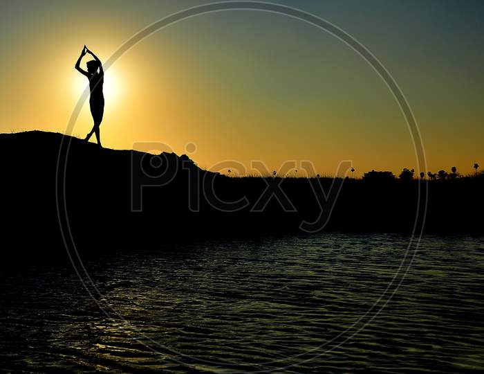 Silhouette of a boy doing yoga while the sunrise