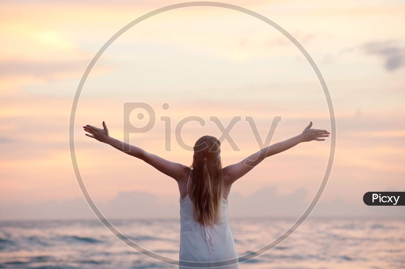 Rear View of Woman With Arms Raised at Beach during Sunset.