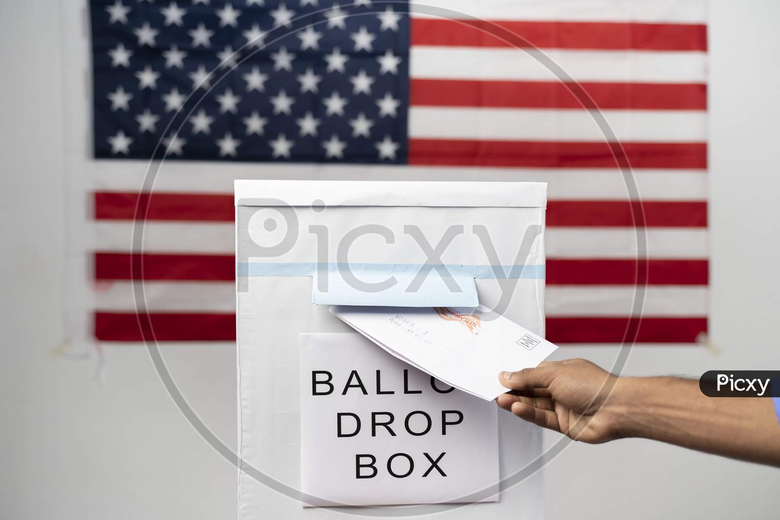 Maski, India 14 September, 2020 : Concept Of Mail In Vote At Us Election - Wide Angle Shot Of Hands Dropping Mail Inside The Ballot Box With Us Flag As Background.