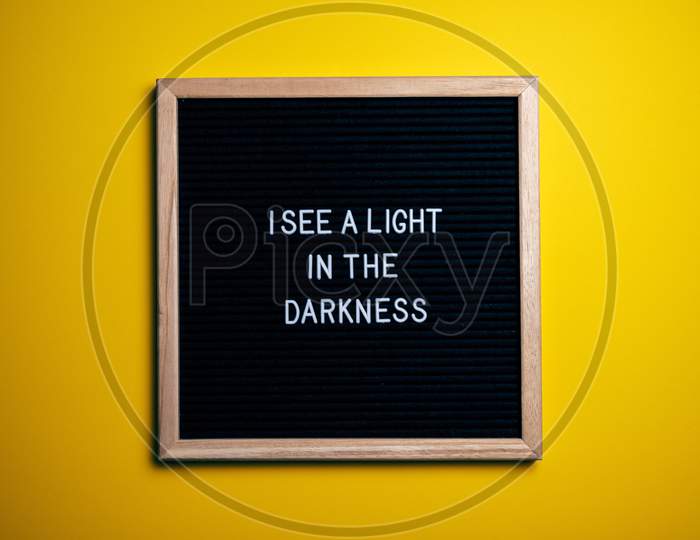 Motivational Quote "I SEE A LIGHT IN THE DARKNESS " Text In The Black Slate Behind Yellow Background.