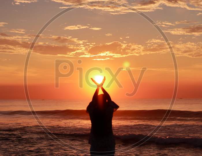A Young Woman Silhouette, Raising Her Hands Towards The Sky, Standing On The Sea Shore At Sunrise In The Morning, Expressing Her Welcome And Gratitude To The Sun