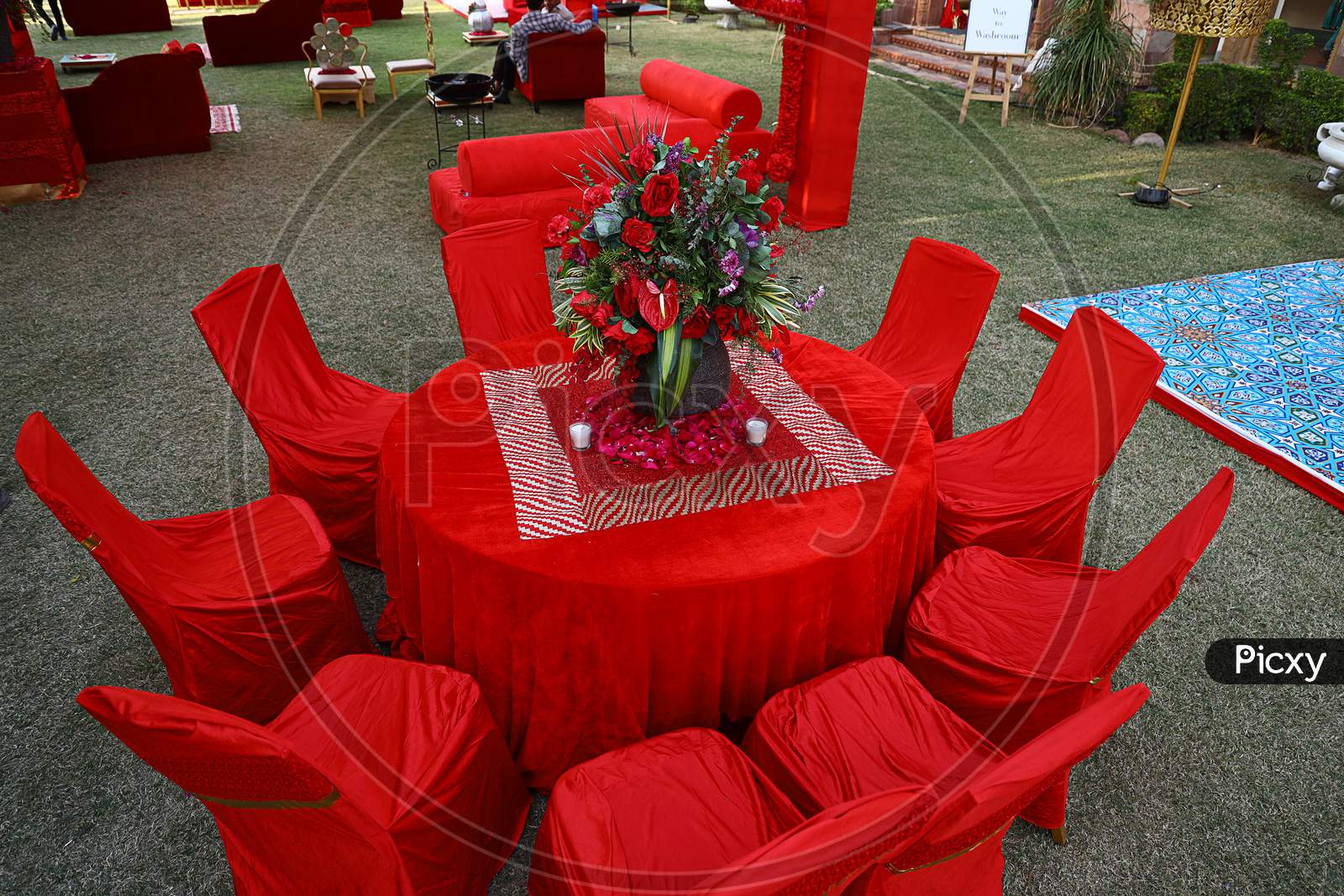 Organized Red Table And Chairs Decorated With Flower Centerpiece, Luxury Sitting Arrangement Ready For The Guests On A Grassland Or Backyard
