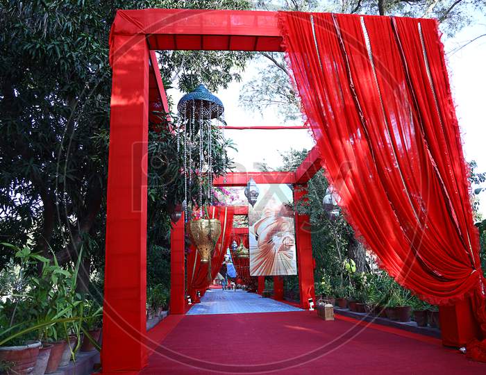 Colorful Decorated Outdoor Entrance Gate At Wedding Scene With Red Curtains And Chandelier, Park Or Lawn Background, Indian Wedding Or Reception Destination