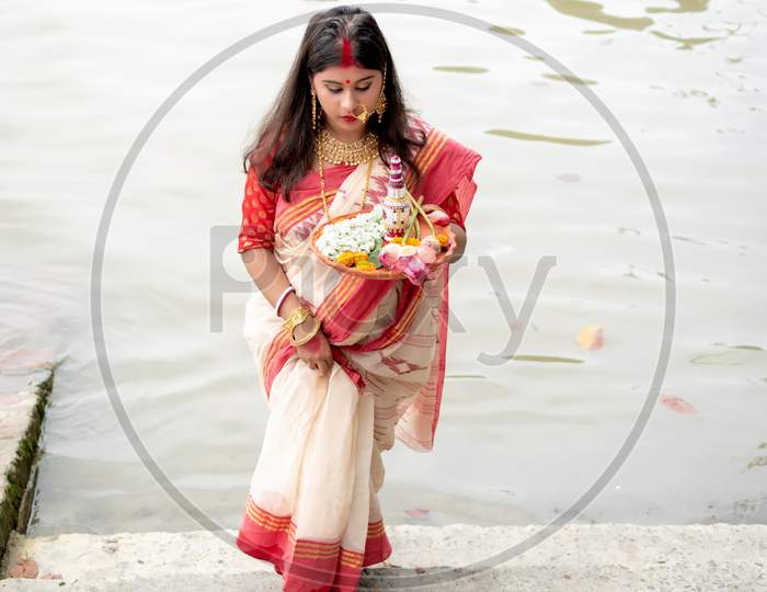 Portrait Of Beautiful Indian Girl Wearing Traditional Indian Saree, Gold Jewellery And Bangles Holding Plate Of Religious Offering In Kolkata, India On September 2020