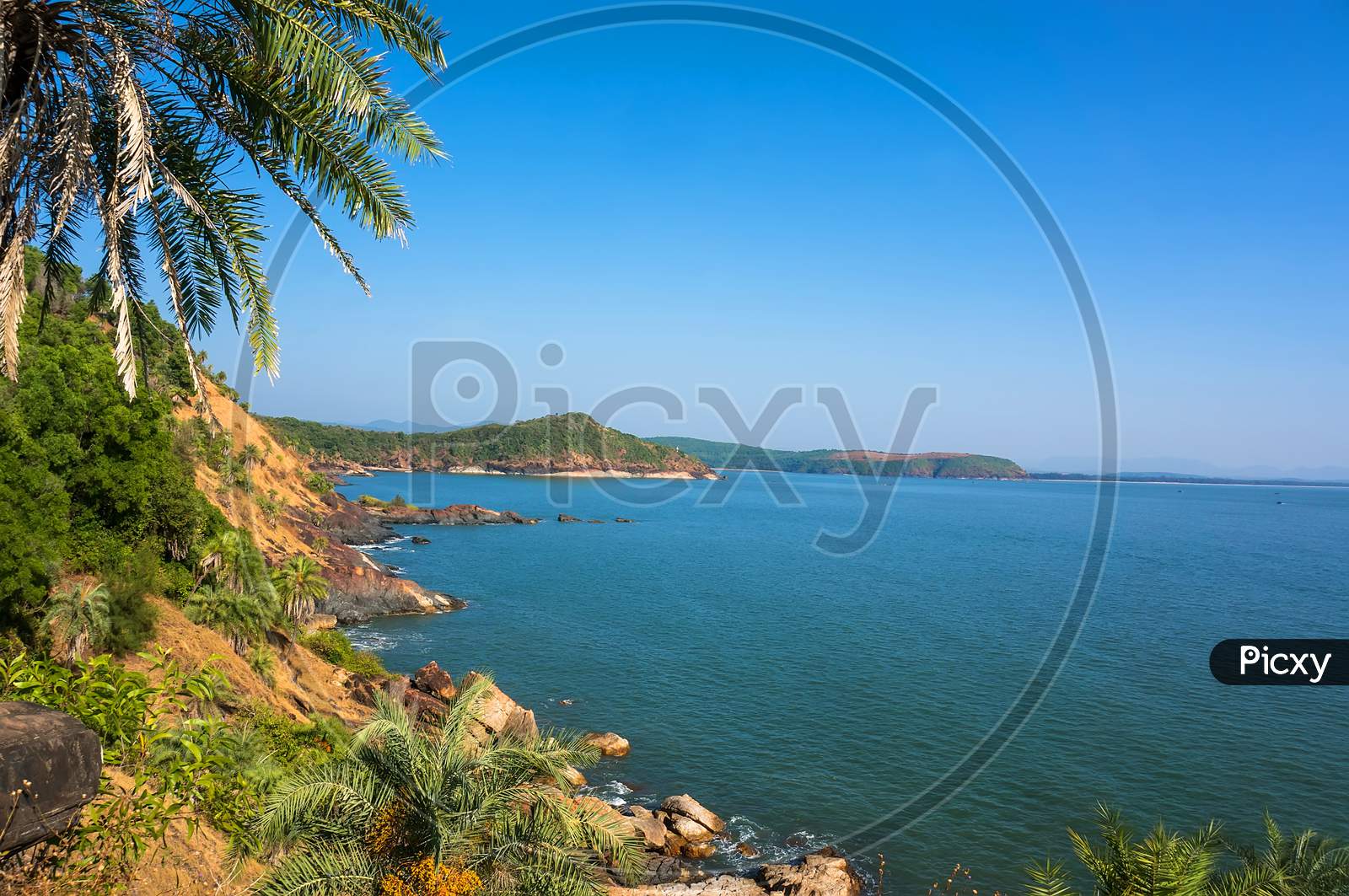 The Scenery Is Beautiful Rocky Coast With Palm Tree, Blue Sea And Cloudless Sky In Om Beach, Karnataka, India