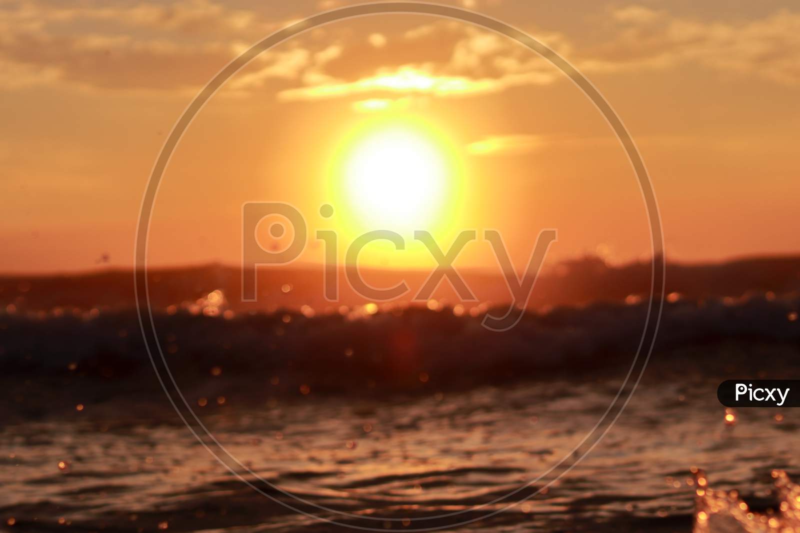 A Defocused Background In Which A Which Bright Round Sun Rises Above The Sky With The Rising Waves Of The Sea