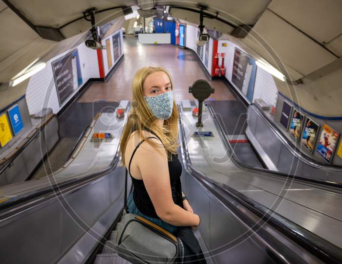 Blonde Female Wearing A Ppe Face Mask Traveling On An Escalator At A London Underground Tube Station