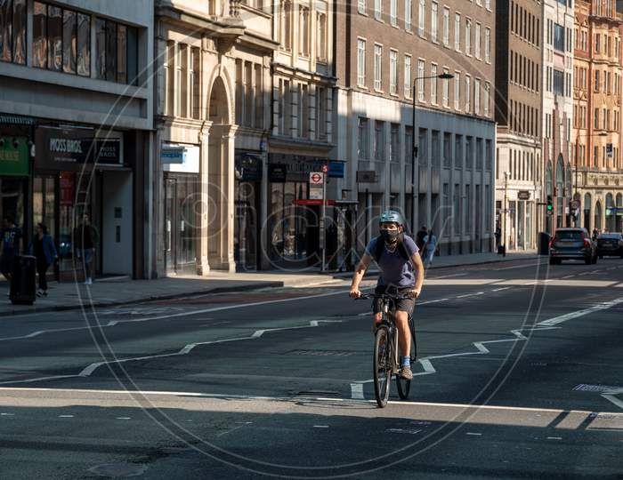 Man Riding Bicycle Along A Quiet London Street And Wearing A Ppe Face Mask During Covid 19 Pandemic
