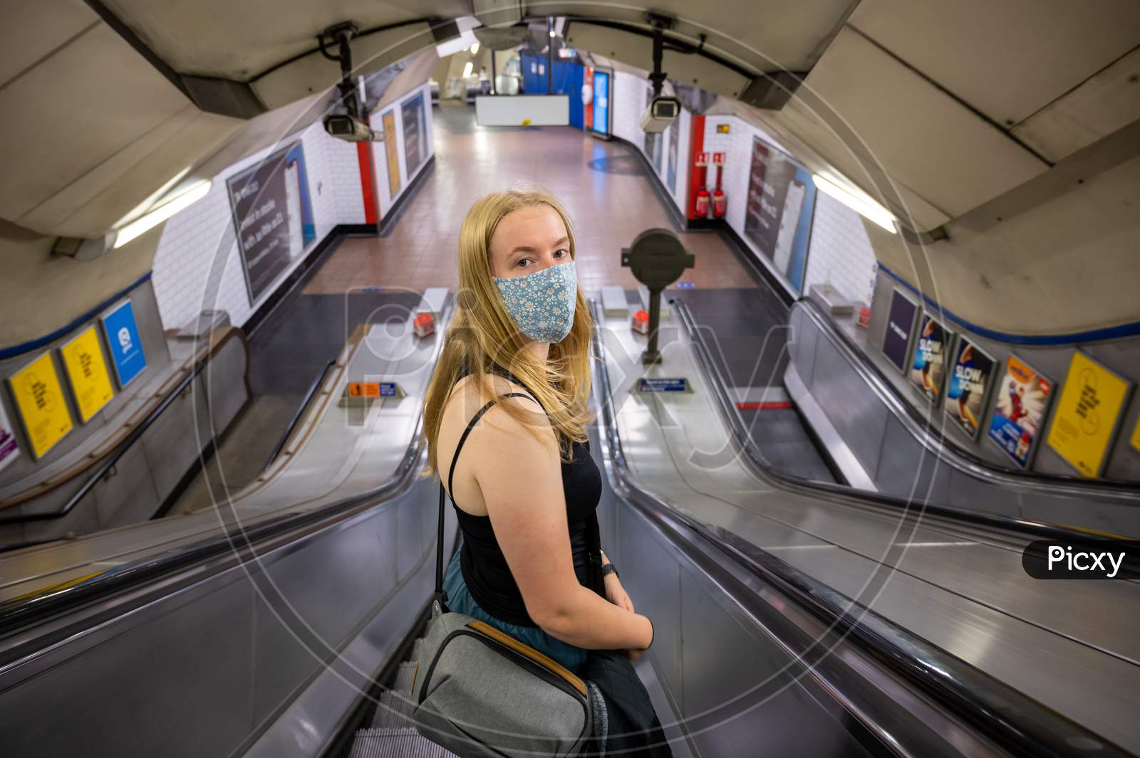 Blonde Female Wearing A Ppe Face Mask Traveling On An Escalator At A London Underground Tube Station