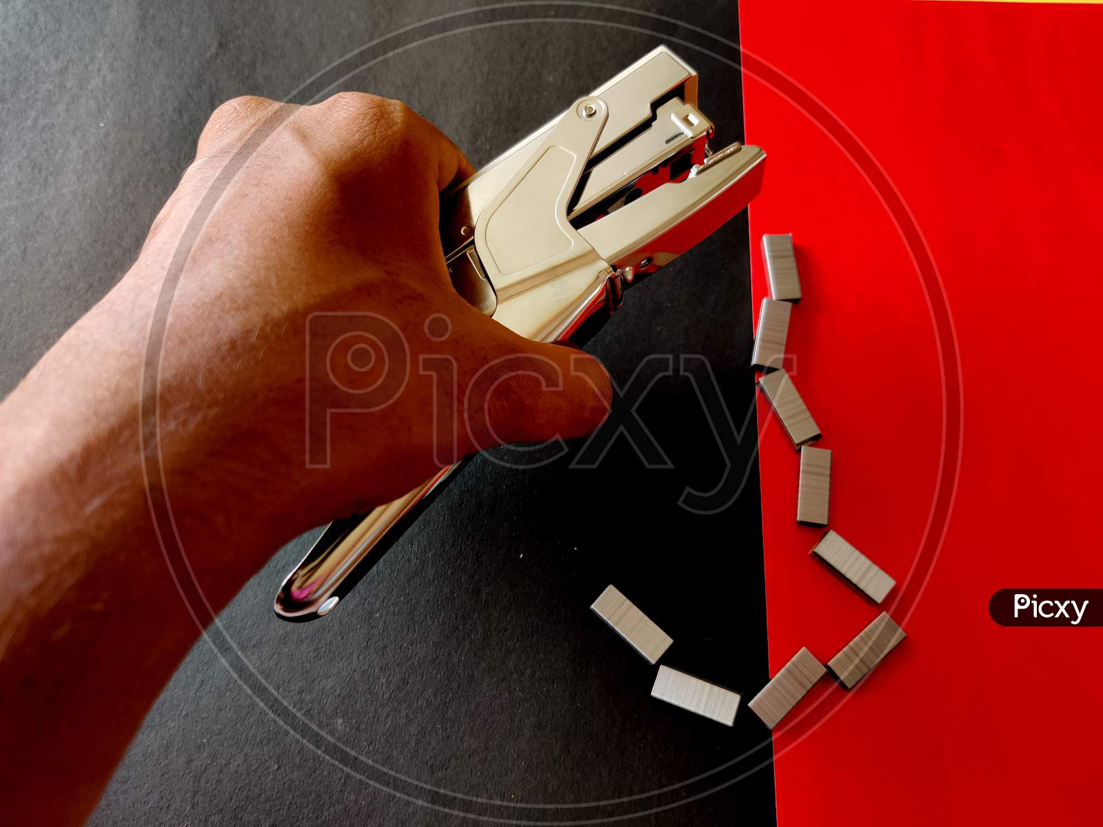 Human Hand Picking Up Big Stapler. Isolated On Red Background.