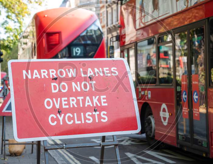 Narrow Lanes Road Traffic Sign Protecting Cyclists, With Red London Double Decker Buses Passing In The Background