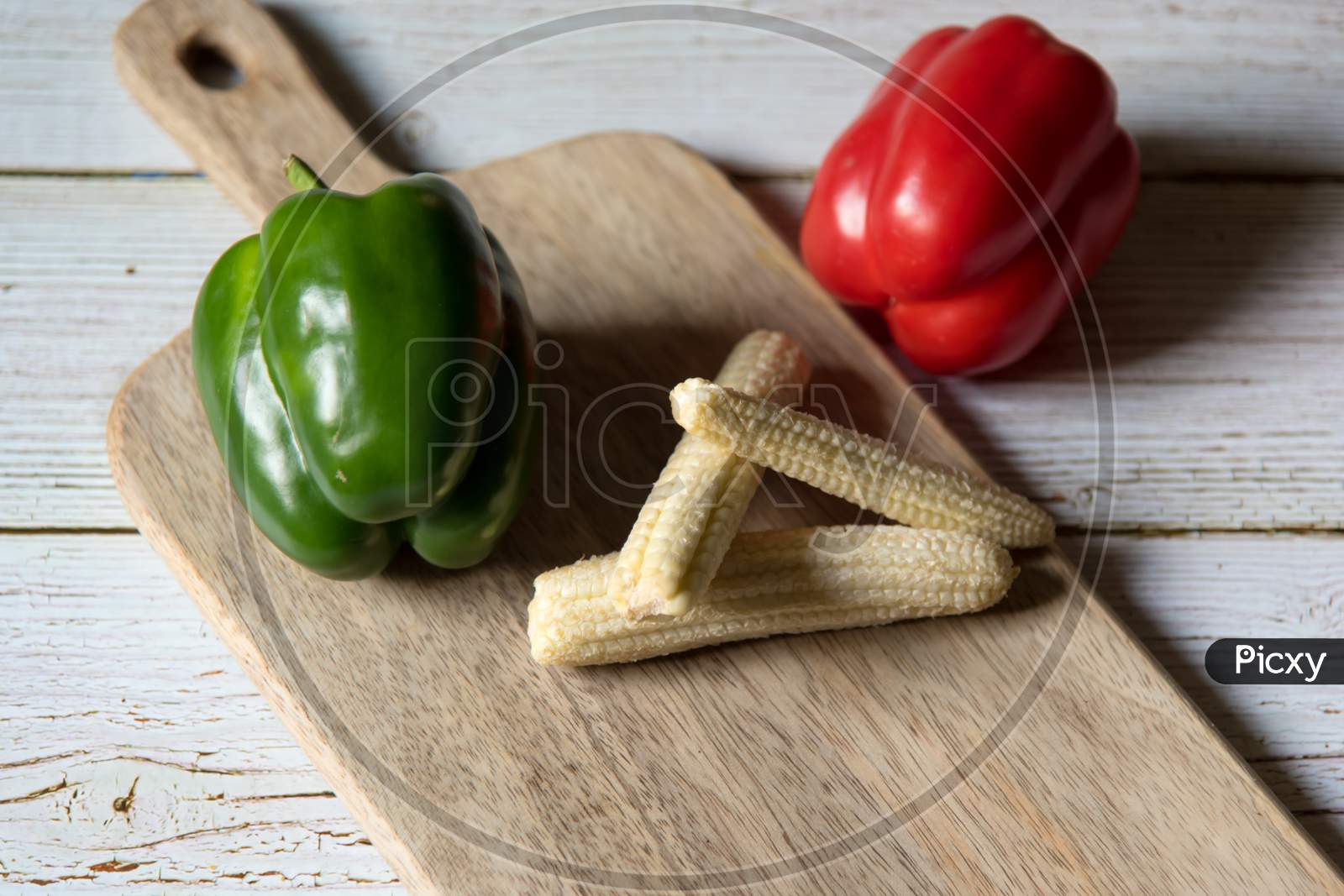 Close up of red and green  bell pepper along with baby corns on a wooden platter