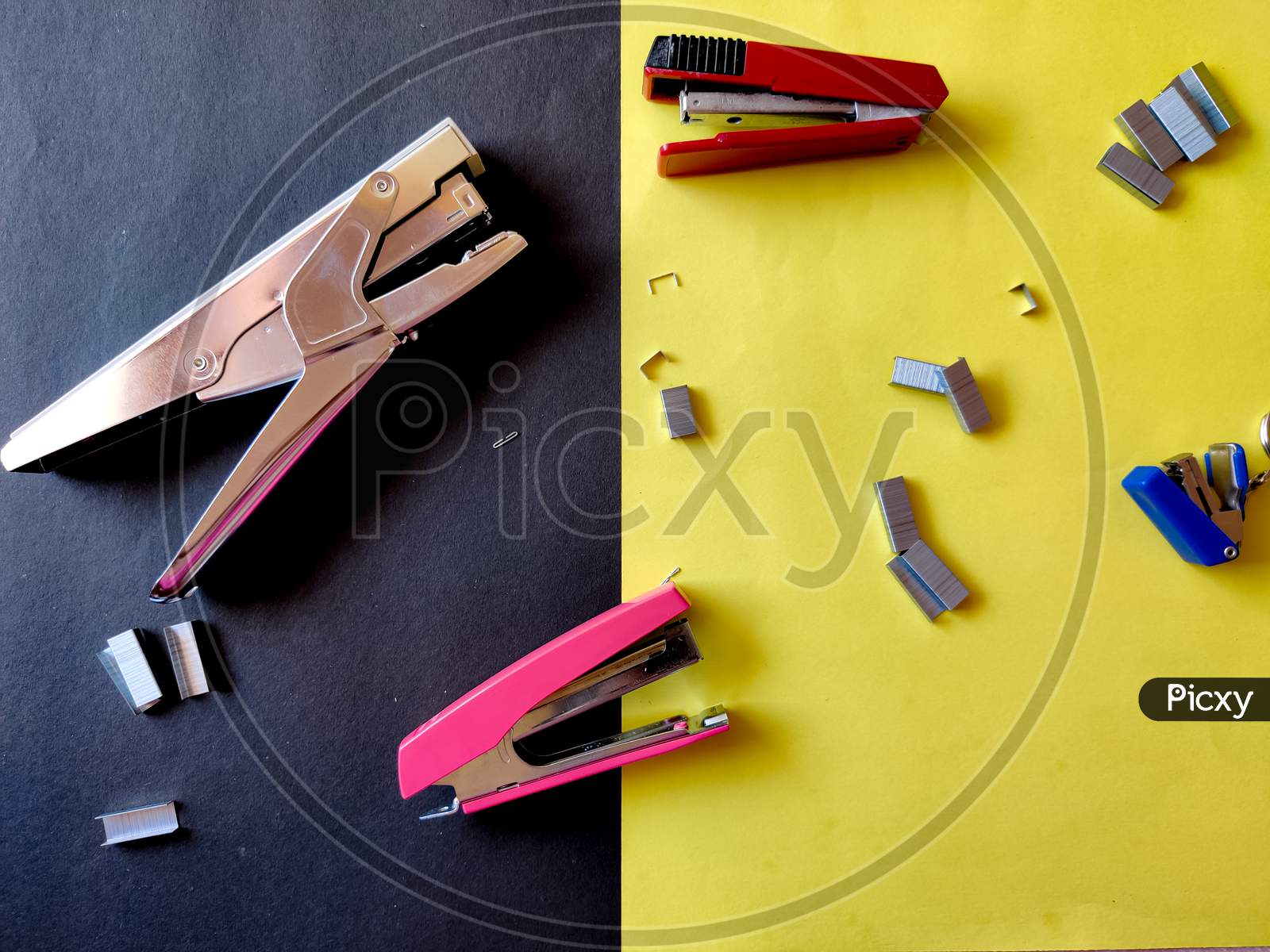 Four Different Sized Staplers And Stapler Pins Isolated On Yellow Background. Top View