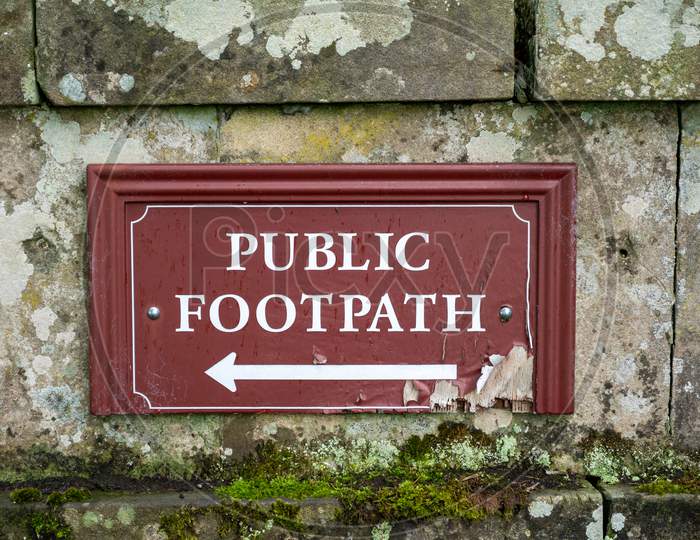 Head On View Of An Old Distressed Public Footpath Sign On An Old Stone Wall