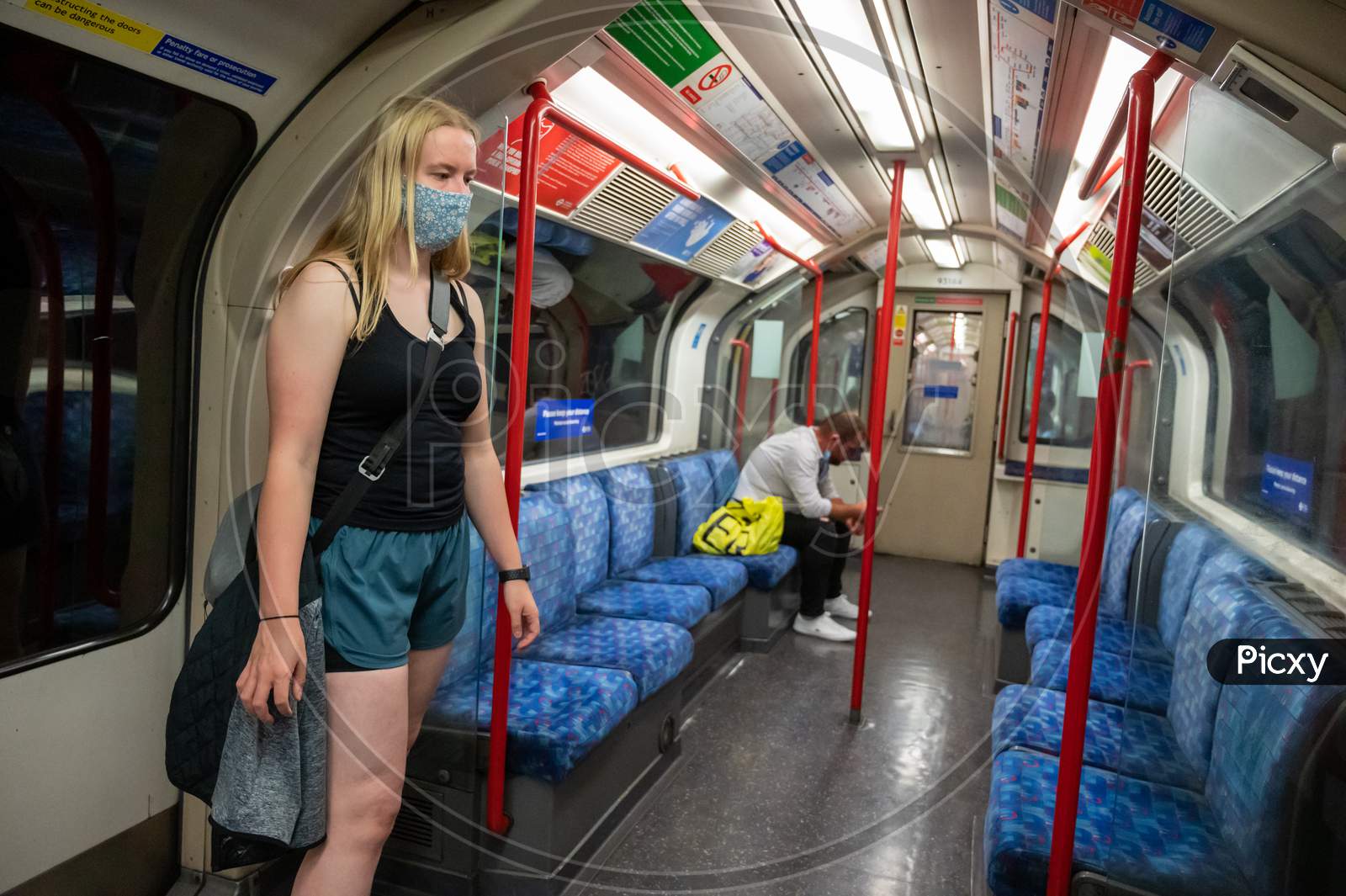 Blonde Female Wearing A Ppe Face Mask Traveling On An Almost Empty London Underground Tube Train