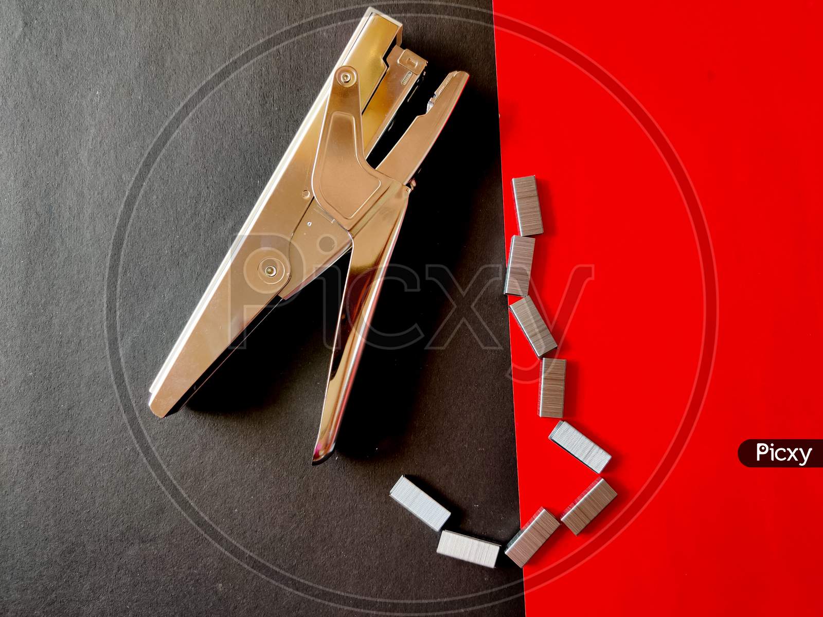 Silver Color Big Stapler And Stapler Pins Isolated On Red Background.