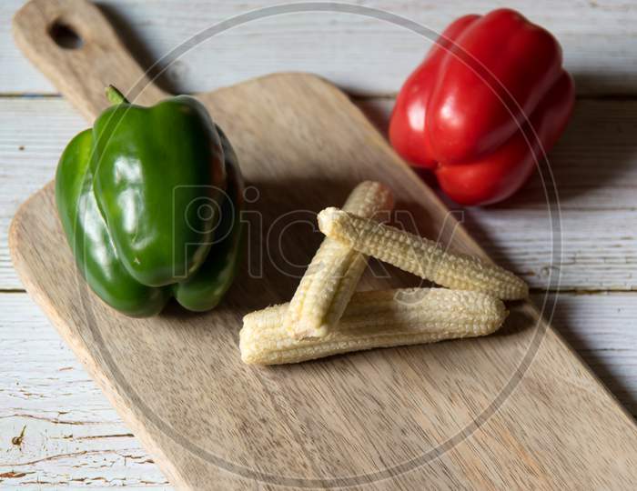 Close up of red and green  bell pepper along with baby corns on a wooden platter