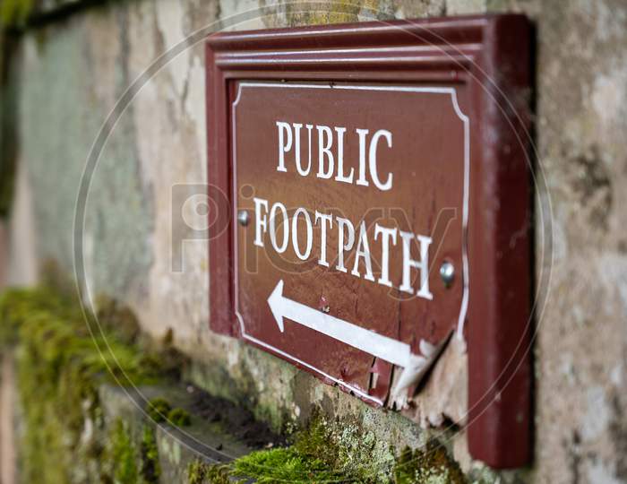 Close Up View Of An Old Distressed Public Footpath Sign On A Moss Covered Old Stone Wall
