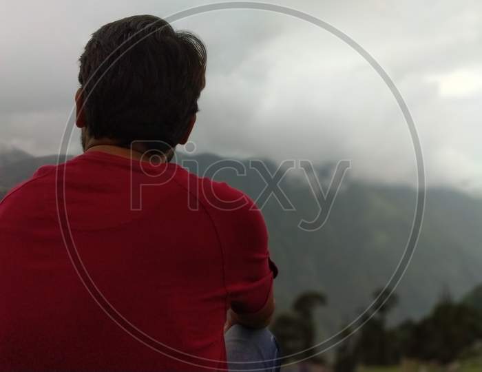 Young man is sitting on cliff's edge and enjoying the view in in India Mountains Himalayas Dharamshala Triund Himachal Pradesh. Mountaineering sport lifestyle concept