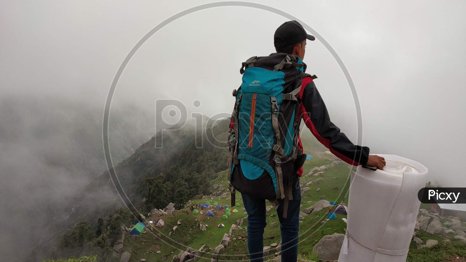Hiker with backpack standing on top of a mountain and enjoying the view in India Mountains Himalayas Dharamshala Triund Himachal Pradesh