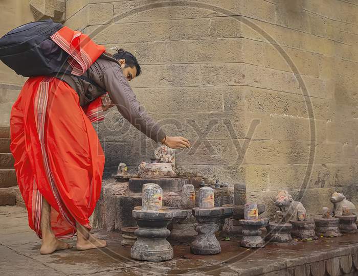 A pilgrim dressed in red doing its prayers at lingams on the river Ganges in Varanasi, India