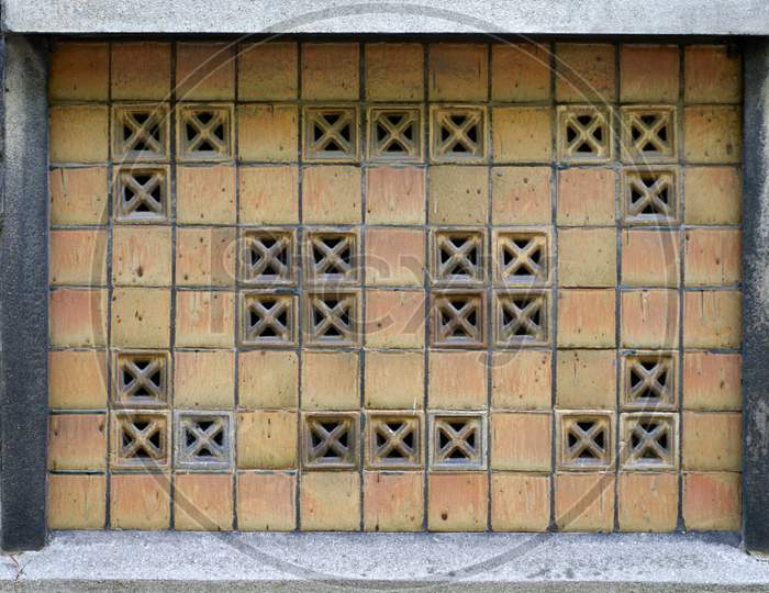 A Window Made Up Of Concrete Along With Some Square Holes With Cross Pattern In It