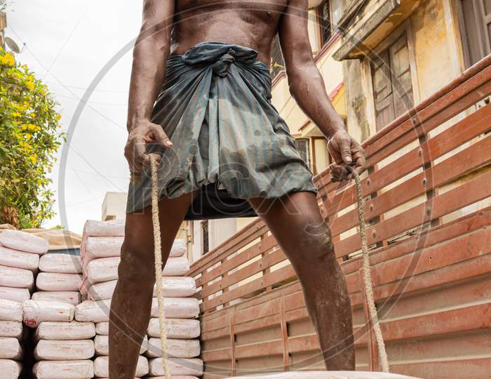 Indian Construction Worker Looking At Camera And Smiling Before Lifting A Sack Of Cement