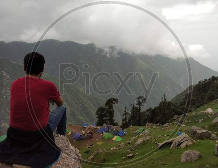 Young man is sitting on cliff's edge and enjoying the view in in India Mountains Himalayas Dharamshala Triund Himachal Pradesh. Mountaineering sport lifestyle concept
