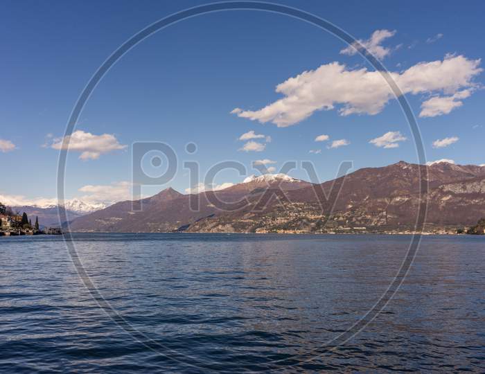 Italy, Lecco, Lake Como, A Large Body Of Water With A Mountain In The Background