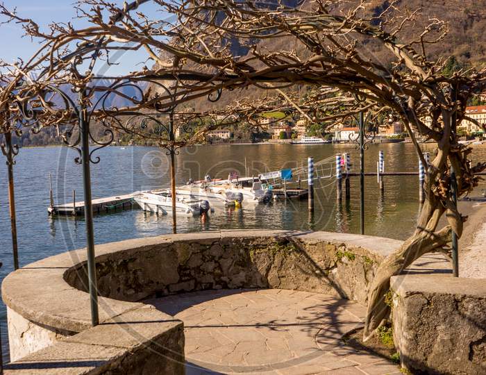 Italy, Menaggio, Lake Como, A Stone Bridge Over A Body Of Water