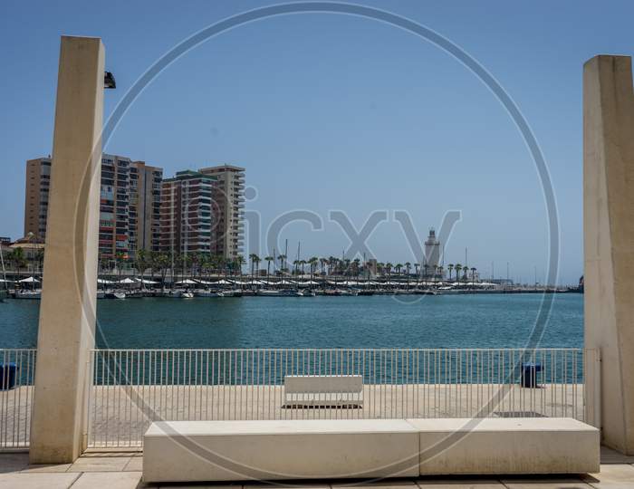 The Sea And The Lighthouse Viewed Through Two Pillars At Malaga, Spain, Europe On A Bright  Summer Day
