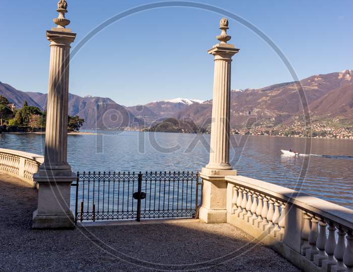Italy, Bellagio, Lake Como, Fence Overlooking Scenic View Of Snowcapped Mountains Against Blue Sky, Lombardy
