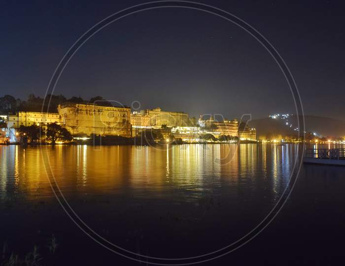 Photograph of famous city palace udaipur with its light reflection on the bank of lake pichola udaipur.